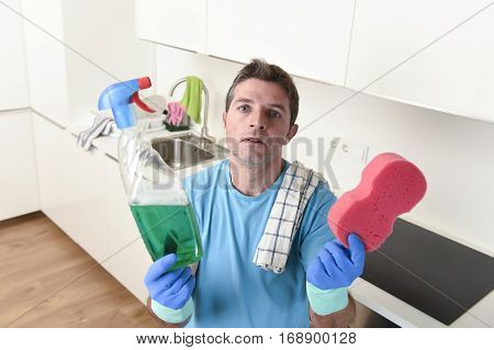 young lazy house cleaner man washing and cleaning the kitchen with detergent spray bottle and sponge in stress and desperate face expression in male housework and housekeeping concept