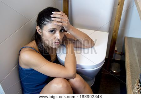 young sad and depressed bulimic woman feeling sick sitting at the floor of the toilet leaning on WC in sickness hangover alcohol abuse and nutrition disorder bulimia concept