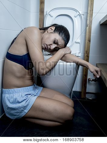 young sad and depressed bulimic woman feeling sick sitting at the floor of the toilet leaning on WC in sickness hangover alcohol abuse and nutrition disorder bulimia concept