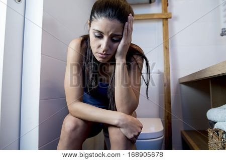 young sad and depressed bulimic woman feeling sick sitting in toilet WC looking desperate and ill in pregnancy and depression concept