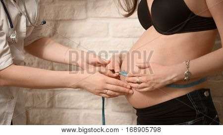Friendly Female Medicine Doctor Holding Centimeter Tape And Listening To Pregnant Woman Standing For