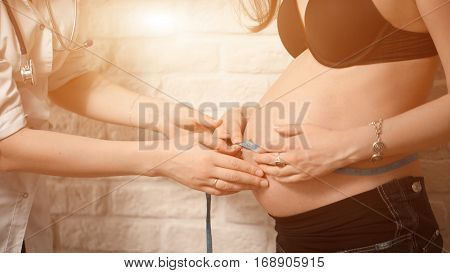 Friendly Female Medicine Doctor Holding Centimeter Tape And Listening To Pregnant Woman Standing For