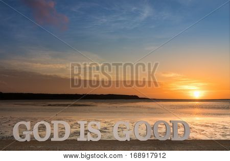 3D words saying 'lGod is good' as the sun goes down into clouds over a river lagoon.