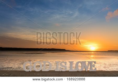 3D words saying 'God is love' as the sun goes down over a river lagoon.