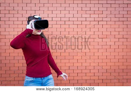Handsome young woman using VR glasses with brickwall background and space for text