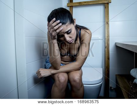 young sad and depressed bulimic woman feeling sick sitting in toilet WC looking desperate and ill in pregnancy and depression concept