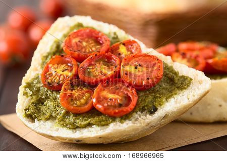 Olive bread roll halves spread with basil pesto and topped with roasted cherry tomato halves photographed with natural light (Selective Focus Focus in the middle of the bread roll half)