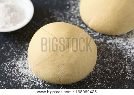 Risen or proved yeast dough balls for bread or pizza on a floured slate surface photographed with natural light (Selective Focus Focus on the front of the dough ball)