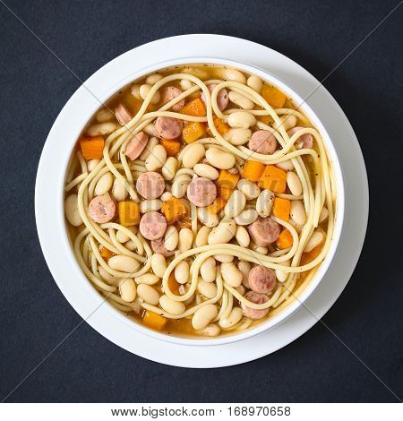 Chilean traditional Porotos con Riendas (beans with reins) dish of cooked dried beans with pumpkin onion spaghetti and sausage photographed overhead on slate with natural light