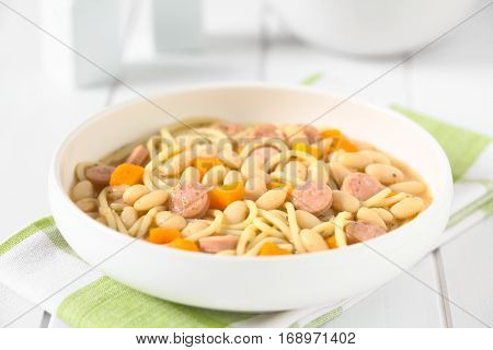 Chilean traditional Porotos con Riendas (beans with reins) dish of cooked dried beans with pumpkin onion spaghetti and sausage photographed on white wood with natural light (Selective Focus Focus one third into the dish)