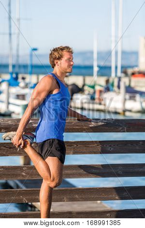 Athlete man stretching legs before running in San Francisco bay harbor - city lifestyle. Fitness runner doing warm-up before cardio workout.