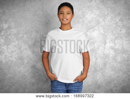 Young African American boy in blank white t-shirt standing against textured wall