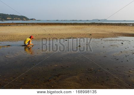 Quang Ninh, Vietnam - May 1, 2012: A boy working on beach when tide going out, rake black sand to catch sell fish. There are a lot of children labors in country