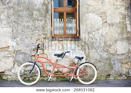 Modern Comfortable Orange Tandem Double Bicycle With White Wheels Leaned To The Old Plastered Cracke
