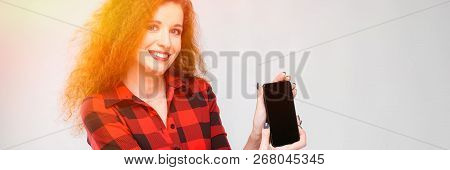Young Red-haired Girl In A Red Checkered Shirt. Young Girl Shows Phone