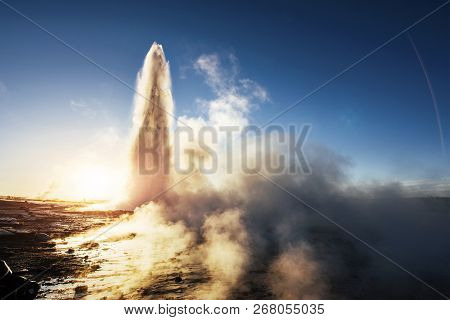 Eruption Of Strokkur Geyser In Iceland. Winter Cold Colors, Sun Lighting Through The Steam