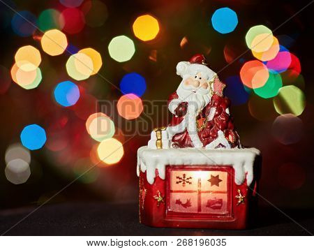 Santa Claus Statuette Doing An Exercise Waiting For Christmas. Colored Bokeh