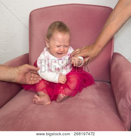 Crying Baby Sitting In The Chair. Hands Of Grandmother Holding Child Sitting In The Chair. Negative 