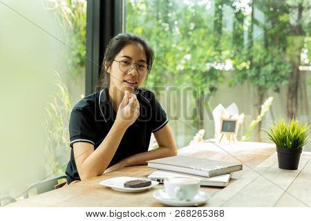 Asiam Woman Student Eating Cake With Book And Laptop In Coffee Shop.
