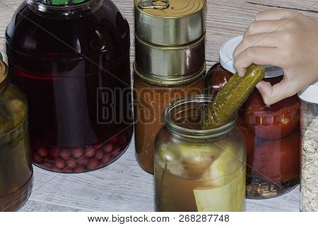 Hand Reaching For Pickled Cucumber. Storage Shelves In Pantry With Homemade Canned Preserved Fruits 