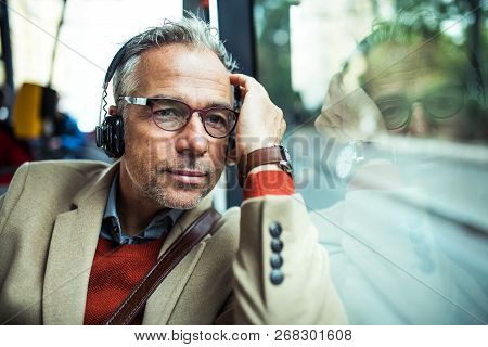 Mature Tired Businessman With Heaphones Travelling By Bus In City.