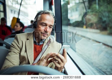Mature Tired Businessman With Heaphones And Smartphone Travelling By Bus In City.
