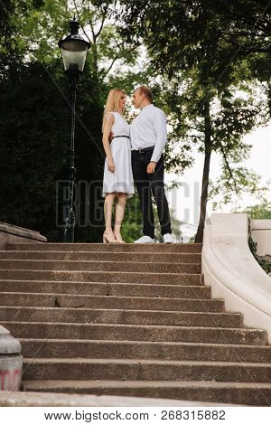 Beautiful Cuple Stand On The Stairs And Hug Each Other. Man And Woman Walking In The Park. Lovestory