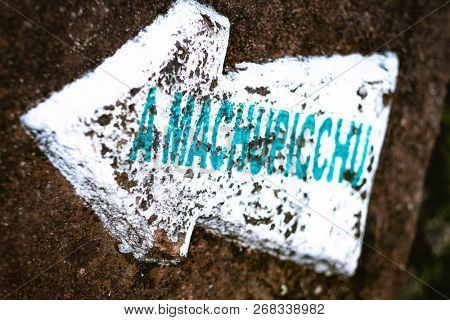 Closeup of white pointing arrow sign to Machupicchu with blue label on the rock