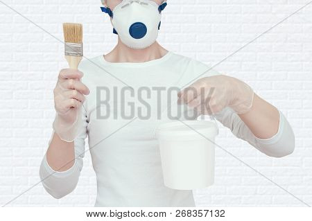 The Girl Is Holding A Bucket Of Paint And A Brush For Painting. On A Bricky White Wall Background.