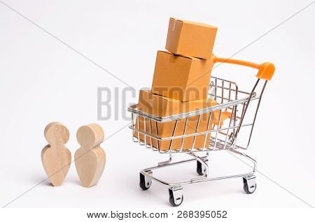 People Stand And Talk Near The Trade Wheelbarrow With Cardboard Boxes. Services For The Transportati