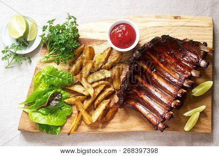 Homemade Baked Meat Ribs Served With French Fries, Herbs, Lime And Ketchup On A Wooden Board. Rustic