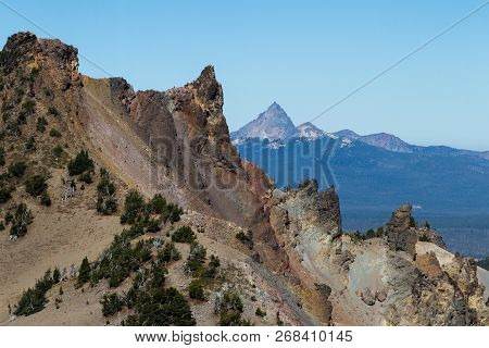 Rocky Spires And Crumbling Rocks At The Top Of Crater Lake With Mount Thielsen In The Background
