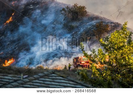 Two Firefighters Next To Red Bulldozer With Burning Hillside In Background During California Brushfi