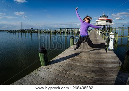 Beautiful Woman Jumps On A Dock Alongside The Choptank River Lighthouse In Maryland