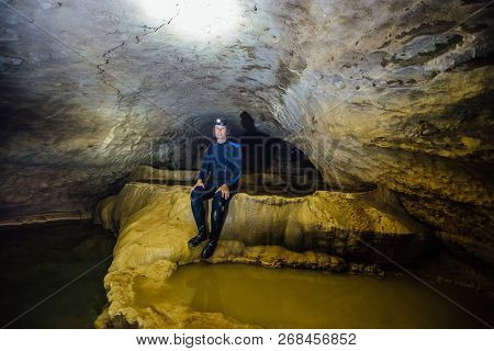 Happy Man Tourist  Speleologist In Wetsuit With Led Headlight In Beautiful Natural Cave With Cascade