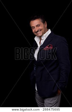 Emotional Optimistic Businessman Standing Against The Black Background With His Hands In The Pockets