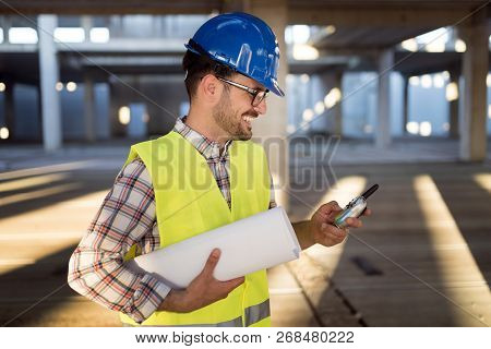 Male Young Architect With Blueprints Using Walkie-talkie