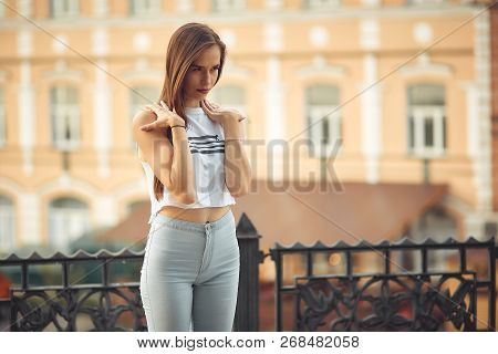 Portrait Of A Girl In Jeans And A T-shirt On The Background Of The Building In The Evening On A Summ