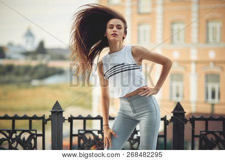 Portrait Of A Girl In Jeans And A T-shirt On The Background Of The Building In The Evening On A Summ