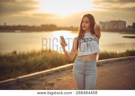Young Beautiful Caucasian Girl Listening To Music With Smartphone Walking In The City With Headphone