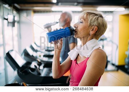 Senior Woman Drinking Bottle Of Water On Threadmill In Gym