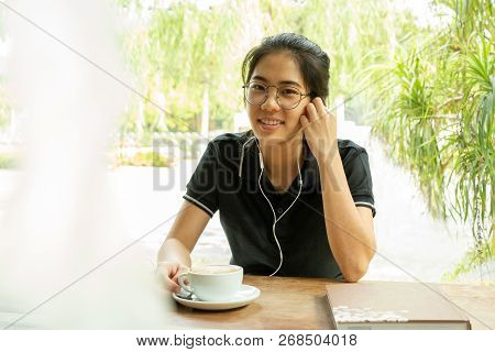 Asian Woman Student Working On Laptop With Earphone Looking At Camera.