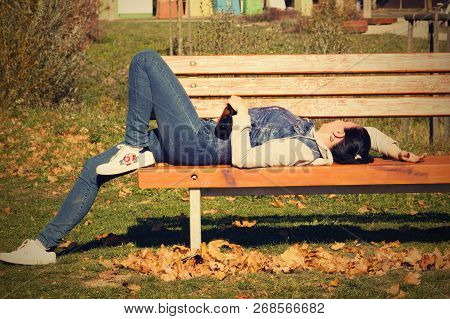 A Drunk Young Woman Sleeping On A Bench In The Day.a Young Woman Holding A Bottle Of Alcohol In Her 
