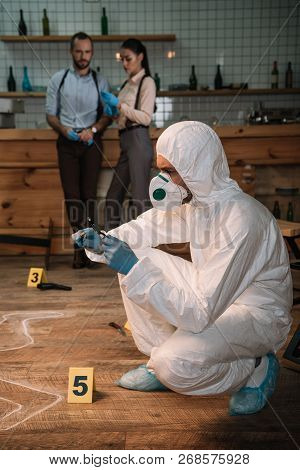Concentarted Forensic Investigator Examining Evidence With Magnifying Glass At Crime Scene With Coll