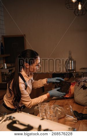Side View Of Concentarted Female Detective Examining Dead Body At Crime Scene
