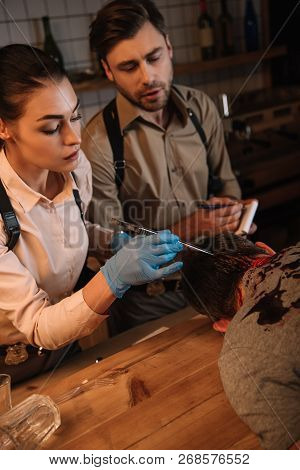 Cropped View Of Concentated Female And Male Detectives Collecting Evidence From Dead Body And Invest