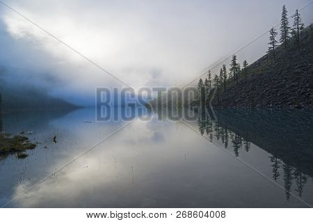 Reflection Of The Shore Of The Lake In The Watery Surface. A Misty Summer Morning. The Large (lower)