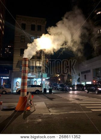 NEW YORK, USA - NOVEMBER 11, 2018: Water condenses in cold night temperatures as warm air exits a drain on a street in Manhattan, New York, USA.