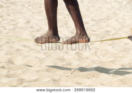 Guy Practising Slack Line On The Beach. Slacklining Is A Practice In Balance That Typically Uses Nyl