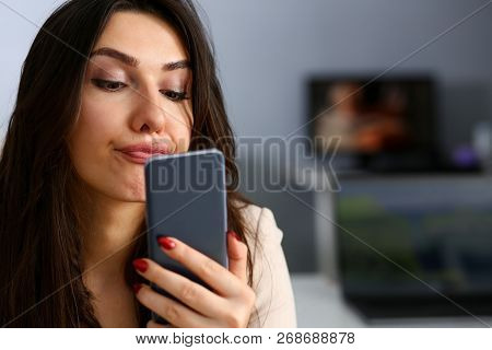 Young Beautiful Businesswoman Unhappily Holding Smartphone In Her Hand Contemptuously Looks At Displ